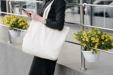 Kentsel şehir arka plan karşı beyaz tekstil eko çanta tutan kadın. Ekoloji veya çevre koruma kavramı. Sahte için beyaz eko çanta.