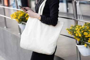 Kentsel şehir arka plan karşı beyaz tekstil eko çanta tutan kadın. Ekoloji veya çevre koruma kavramı. Sahte için beyaz eko çanta.