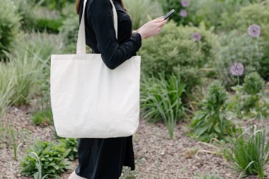 Woman holding white textile eco bag against urban city background. Ecology or environment protection concept. White eco bag for mock up. clipart