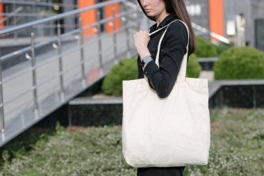 Kentsel şehir arka plan karşı beyaz tekstil eko çanta tutan kadın. Ekoloji veya çevre koruma kavramı. Sahte için beyaz eko çanta.