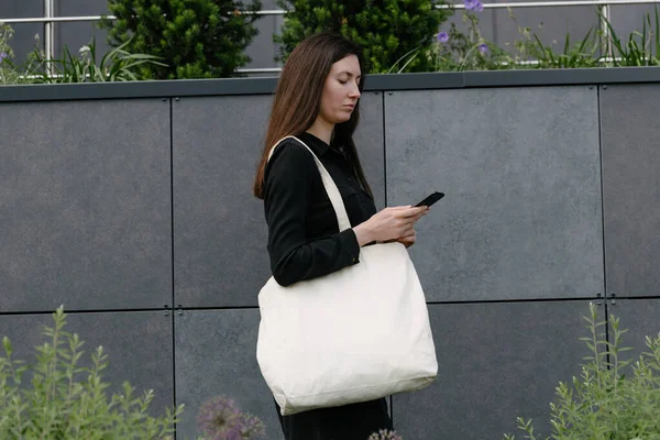都会の背景に白いテキスタイルのエコバッグを持つ女性 エコロジーまたは環境保護の概念 モックアップ用のホワイトエコバッグ — ストック写真