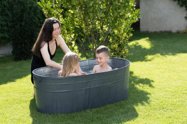 Anne, yazın çocuklarla arka bahçede banyo borusunda eğleniyor.