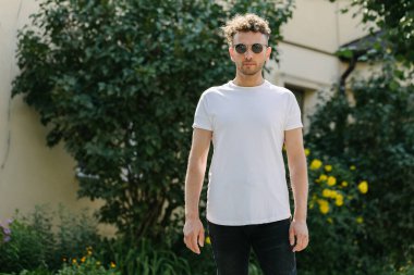 Hippi yakışıklı erkek manken beyaz boş tişört giyiyor. Logonuz için yeri var. Ya da şehir tarzı tasarım.