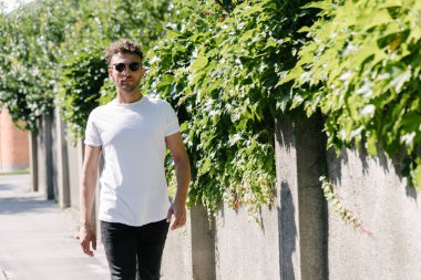 Hippi yakışıklı erkek manken beyaz boş tişört giyiyor. Logonuz için yeri var. Ya da şehir tarzı tasarım.