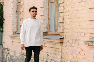 Beyaz sweatshirt ya da kapüşonlu bir adam şehrin sokaklarında boş yeri olan logo tasarımları ya da tasarım baskıları yapıyor..