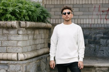 Beyaz sweatshirt ya da kapüşonlu bir adam şehrin sokaklarında boş yeri olan logo tasarımları ya da tasarım baskıları yapıyor..