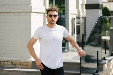 Hippi yakışıklı erkek manken beyaz boş tişört giyiyor. Logonuz için yeri var. Ya da şehir tarzı tasarım.