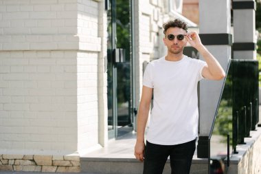 Hippi yakışıklı erkek manken beyaz boş tişört giyiyor. Logonuz için yeri var. Ya da şehir tarzı tasarım.