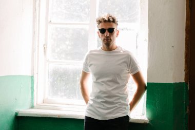 Hippi yakışıklı erkek manken beyaz boş tişört giyiyor. Logonuz için yeri var. Ya da şehir tarzı tasarım.