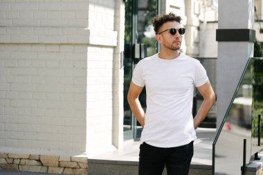 Hippi yakışıklı erkek manken beyaz boş tişört giyiyor. Logonuz için yeri var. Ya da şehir tarzı tasarım.