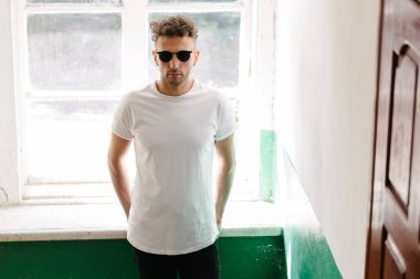 Hippi yakışıklı erkek manken beyaz boş tişört giyiyor. Logonuz için yeri var. Ya da şehir tarzı tasarım.