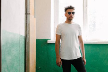 Hippi yakışıklı erkek manken beyaz boş tişört giyiyor. Logonuz için yeri var. Ya da şehir tarzı tasarım.