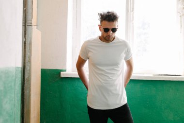 Hippi yakışıklı erkek manken beyaz boş tişört giyiyor. Logonuz için yeri var. Ya da şehir tarzı tasarım.