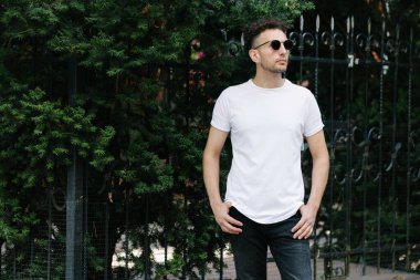 Hippi yakışıklı erkek manken beyaz boş tişört giyiyor. Logonuz için yeri var. Ya da şehir tarzı tasarım.