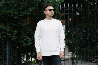 Beyaz sweatshirt ya da kapüşonlu bir adam şehrin sokaklarında boş yeri olan logo tasarımları ya da tasarım baskıları yapıyor..