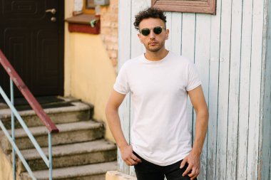 Hippi yakışıklı erkek manken beyaz boş tişört giyiyor. Logonuz için yeri var. Ya da şehir tarzı tasarım.