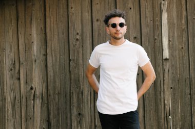 Hippi yakışıklı erkek manken beyaz boş tişört giyiyor. Logonuz için yeri var. Ya da şehir tarzı tasarım.