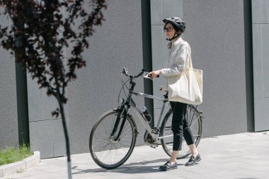 Eko çanta ya da pamuklu çanta taşıyan bir kadın şehirde bisiklet sürerken