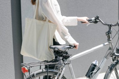 Eko çanta ya da pamuklu çanta taşıyan bir kadın şehirde bisiklet sürerken