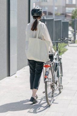 Eko çanta ya da pamuklu çanta taşıyan bir kadın şehirde bisiklet sürerken
