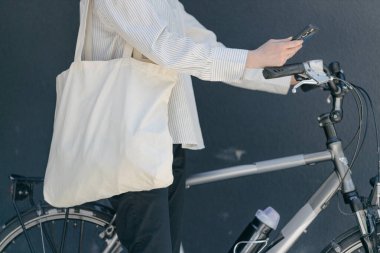 Eko çanta ya da pamuklu çanta taşıyan bir kadın şehirde bisiklet sürerken