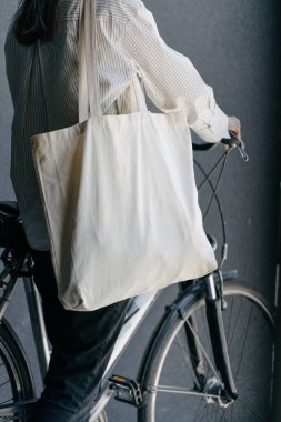 Eko çanta ya da pamuklu çanta taşıyan bir kadın şehirde bisiklet sürerken