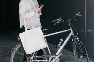 Eko çanta ya da pamuklu çanta taşıyan bir kadın şehirde bisiklet sürerken