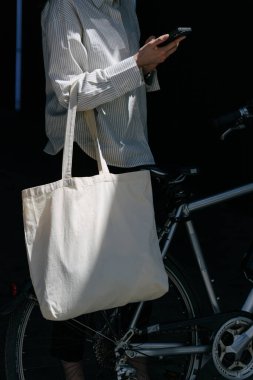 Eko çanta ya da pamuklu çanta taşıyan bir kadın şehirde bisiklet sürerken