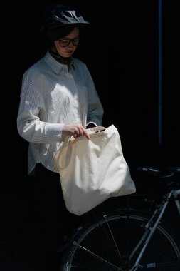 Eko çanta ya da pamuklu çanta taşıyan bir kadın şehirde bisiklet sürerken