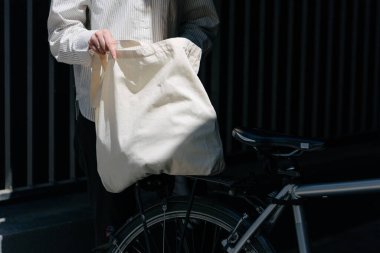 Eko çanta ya da pamuklu çanta taşıyan bir kadın şehirde bisiklet sürerken