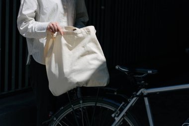 Eko çanta ya da pamuklu çanta taşıyan bir kadın şehirde bisiklet sürerken