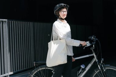 Eko çanta ya da pamuklu çanta taşıyan bir kadın şehirde bisiklet sürerken