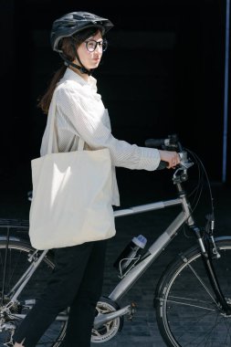 Eko çanta ya da pamuklu çanta taşıyan bir kadın şehirde bisiklet sürerken