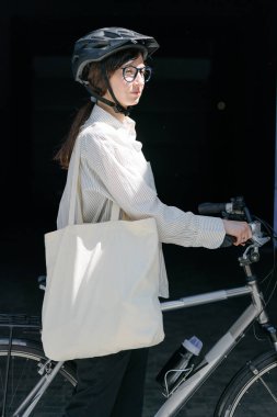 Eko çanta ya da pamuklu çanta taşıyan bir kadın şehirde bisiklet sürerken