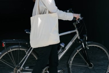 Eko çanta ya da pamuklu çanta taşıyan bir kadın şehirde bisiklet sürerken
