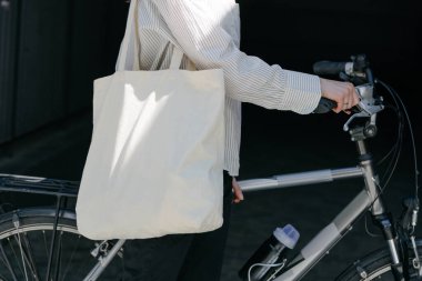 Eko çanta ya da pamuklu çanta taşıyan bir kadın şehirde bisiklet sürerken