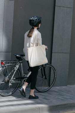 Eko çanta ya da pamuklu çanta taşıyan bir kadın şehirde bisiklet sürerken