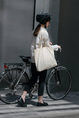Eko çanta ya da pamuklu çanta taşıyan bir kadın şehirde bisiklet sürerken