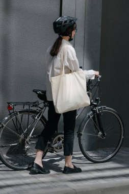Eko çanta ya da pamuklu çanta taşıyan bir kadın şehirde bisiklet sürerken