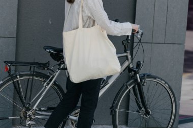 Eko çanta ya da pamuklu çanta taşıyan bir kadın şehirde bisiklet sürerken