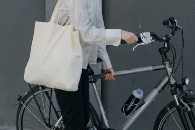 Eko çanta ya da pamuklu çanta taşıyan bir kadın şehirde bisiklet sürerken