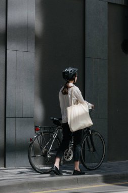 Eko çanta ya da pamuklu çanta taşıyan bir kadın şehirde bisiklet sürerken