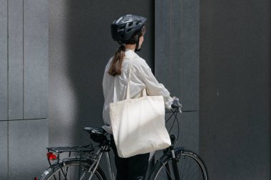 Eko çanta ya da pamuklu çanta taşıyan bir kadın şehirde bisiklet sürerken