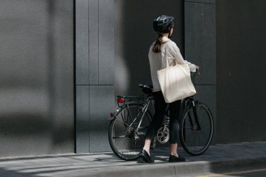 Eko çanta ya da pamuklu çanta taşıyan bir kadın şehirde bisiklet sürerken