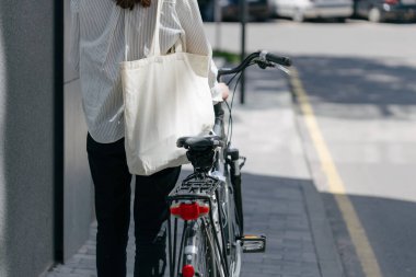 Eko çanta ya da pamuklu çanta taşıyan bir kadın şehirde bisiklet sürerken