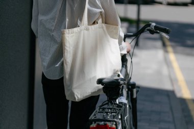 Eko çanta ya da pamuklu çanta taşıyan bir kadın şehirde bisiklet sürerken