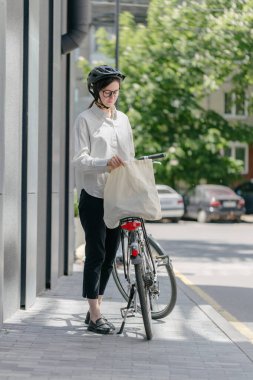 Eko çanta ya da pamuklu çanta taşıyan bir kadın şehirde bisiklet sürerken