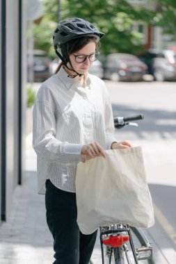 Eko çanta ya da pamuklu çanta taşıyan bir kadın şehirde bisiklet sürerken