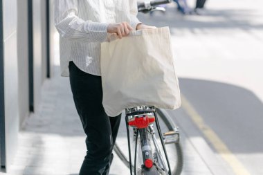 Eko çanta ya da pamuklu çanta taşıyan bir kadın şehirde bisiklet sürerken