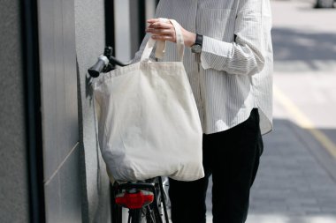 Eko çanta ya da pamuklu çanta taşıyan bir kadın şehirde bisiklet sürerken